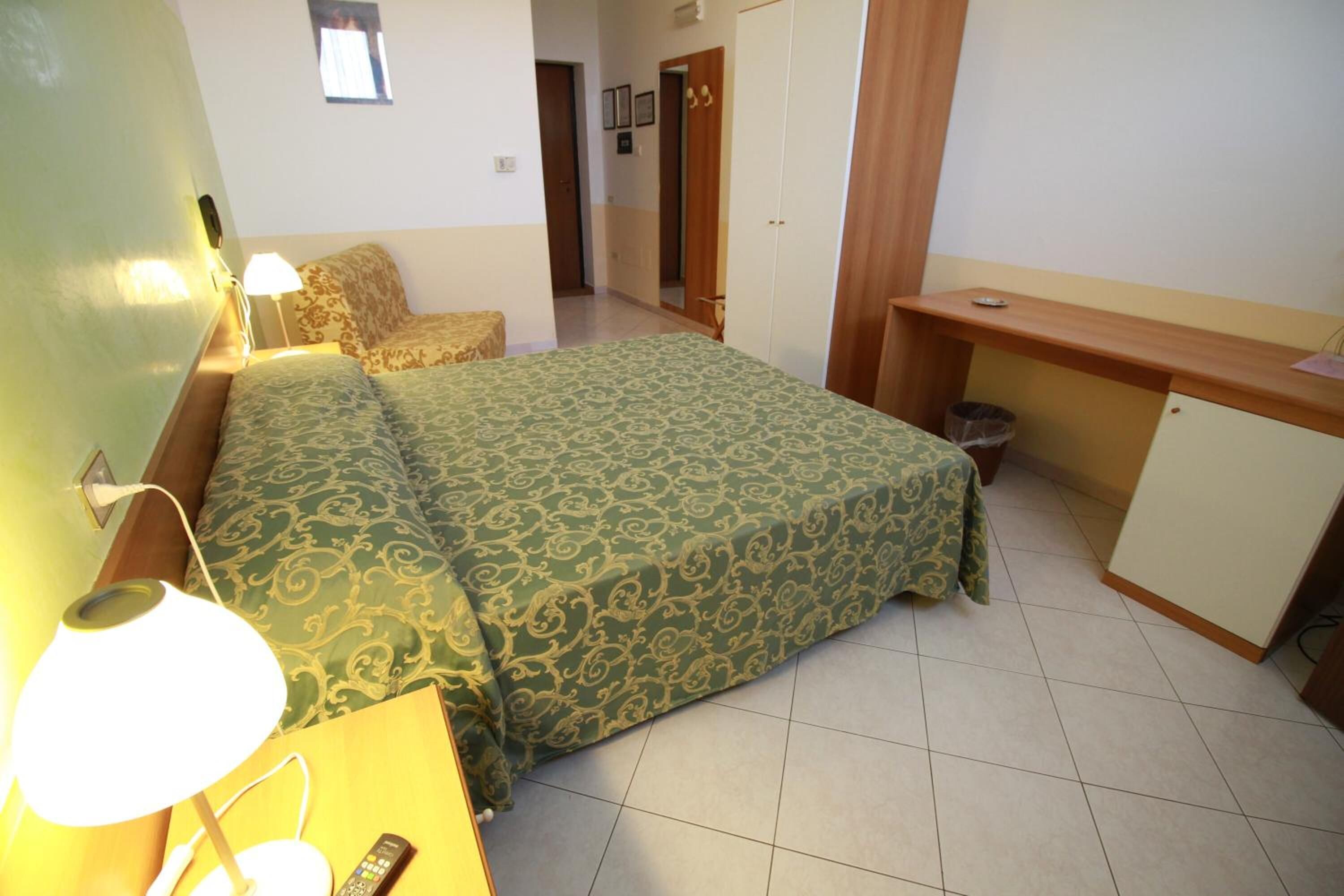 A bedroom with a bed, bedside table, lamp, and a desk with a chair.