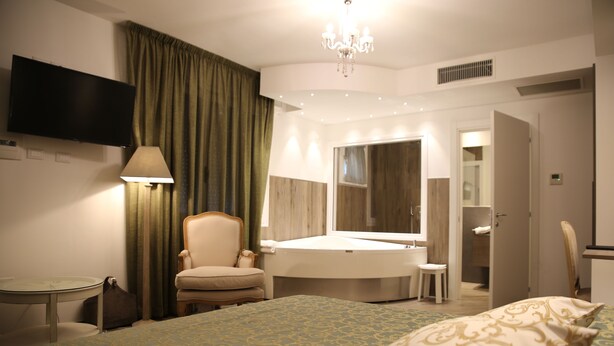 Habitación de hotel con cama, una silla, un escritorio, lámpara, televisor y baño visible a través de una puerta abierta.