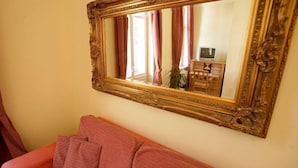 Une pièce avec un grand miroir décoratif, un canapé rose et une commode en bois sur laquelle est posée une télévision.