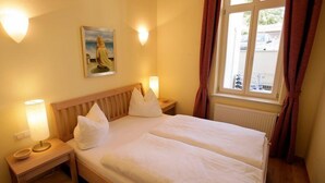 Une chambre d’hôtel avec un lit, deux lampes de chevet, un tableau au mur et une fenêtre avec des rideaux.