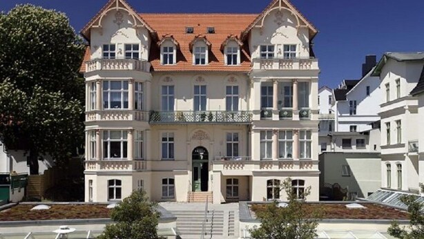 Un grand bâtiment historique à la façade symétrique, doté de nombreuses fenêtres et d’une entrée centrale.