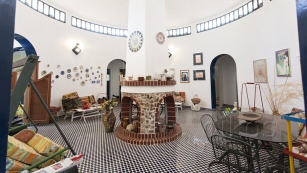 Une pièce spacieuse avec un plafond haut, une cheminée centrale et un coin repas comprenant une table ronde et des chaises.