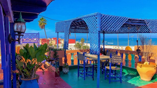 En terrass med en blå pergola, krukväxter och utsikt över stranden och havet.