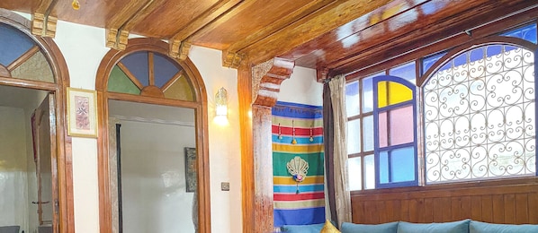 A room with wooden paneling, a large window with decorative iron bars, and a colorful striped curtain. - Dar Statia 3 (El Jadida)