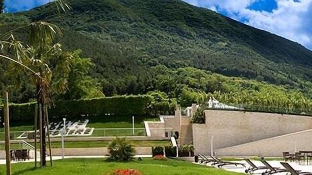 Un hotel moderno con piscina, rodeado de exuberante vegetación y con una montaña de fondo.