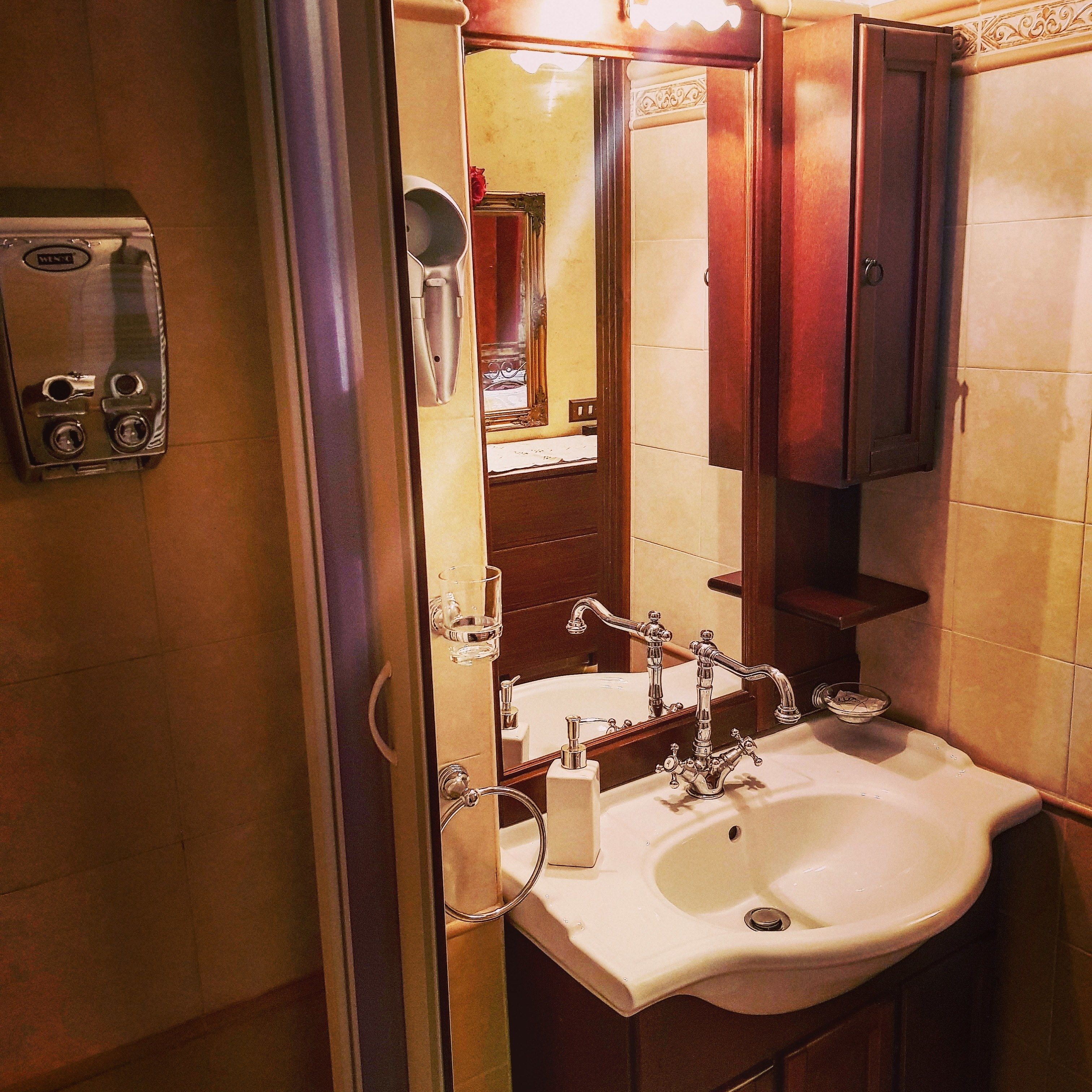 A bathroom with a white sink, a mirror, and a towel dispenser.