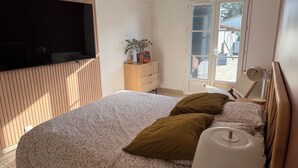 Un dormitorio con cama, cómoda, televisor montado en la pared y ventana con vistas al exterior.