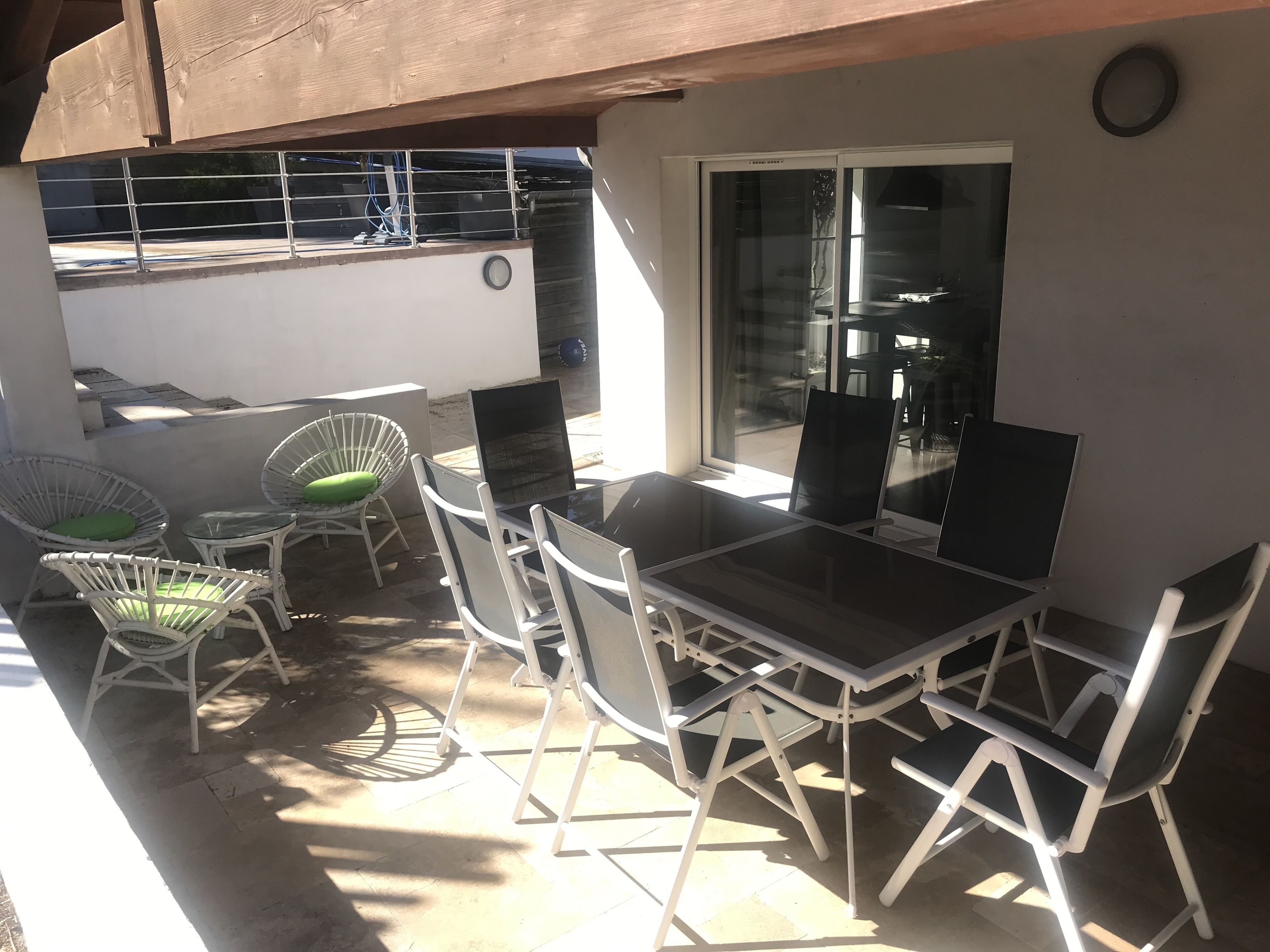 Une terrasse extérieure avec une table et des chaises, une porte vitrée donnant sur l’intérieur et une vue sur la rue.
