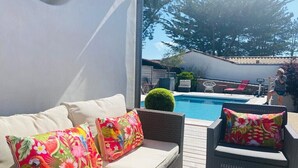 Un área de estar al aire libre con piscina, muebles de mimbre y cojines de colores.