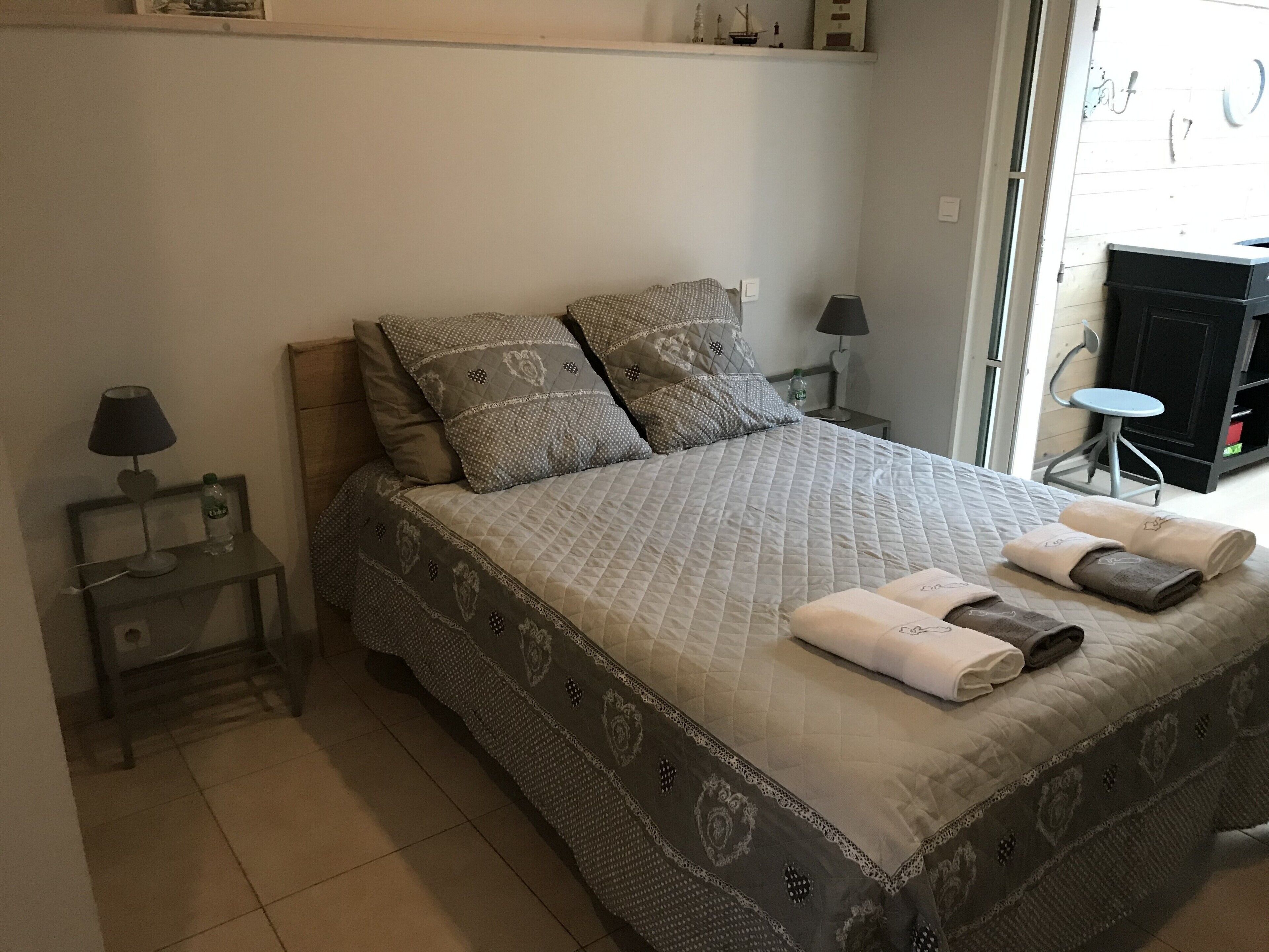 Un lit bien fait, avec une literie à motifs, deux tables de chevet avec des lampes, et une vue sur l’extérieur à travers une porte vitrée.