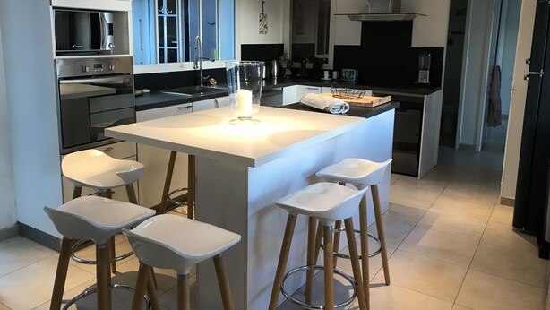 Una cocina moderna con una isla central, taburetes de bar y electrodomésticos de acero inoxidable.