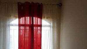 A room with a large window covered by sheer white curtains and a red curtain. - A beautiful and safe 3 bedroom home in a gated community (Mausica)