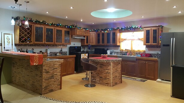 A kitchen with wooden cabinets, a central island with stools, a refrigerator, and a chandelier. - A beautiful and safe 3 bedroom home in a gated community (Mausica)