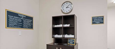 Una habitación con un reloj, un letrero para el gimnasio y un armario con toallas.
