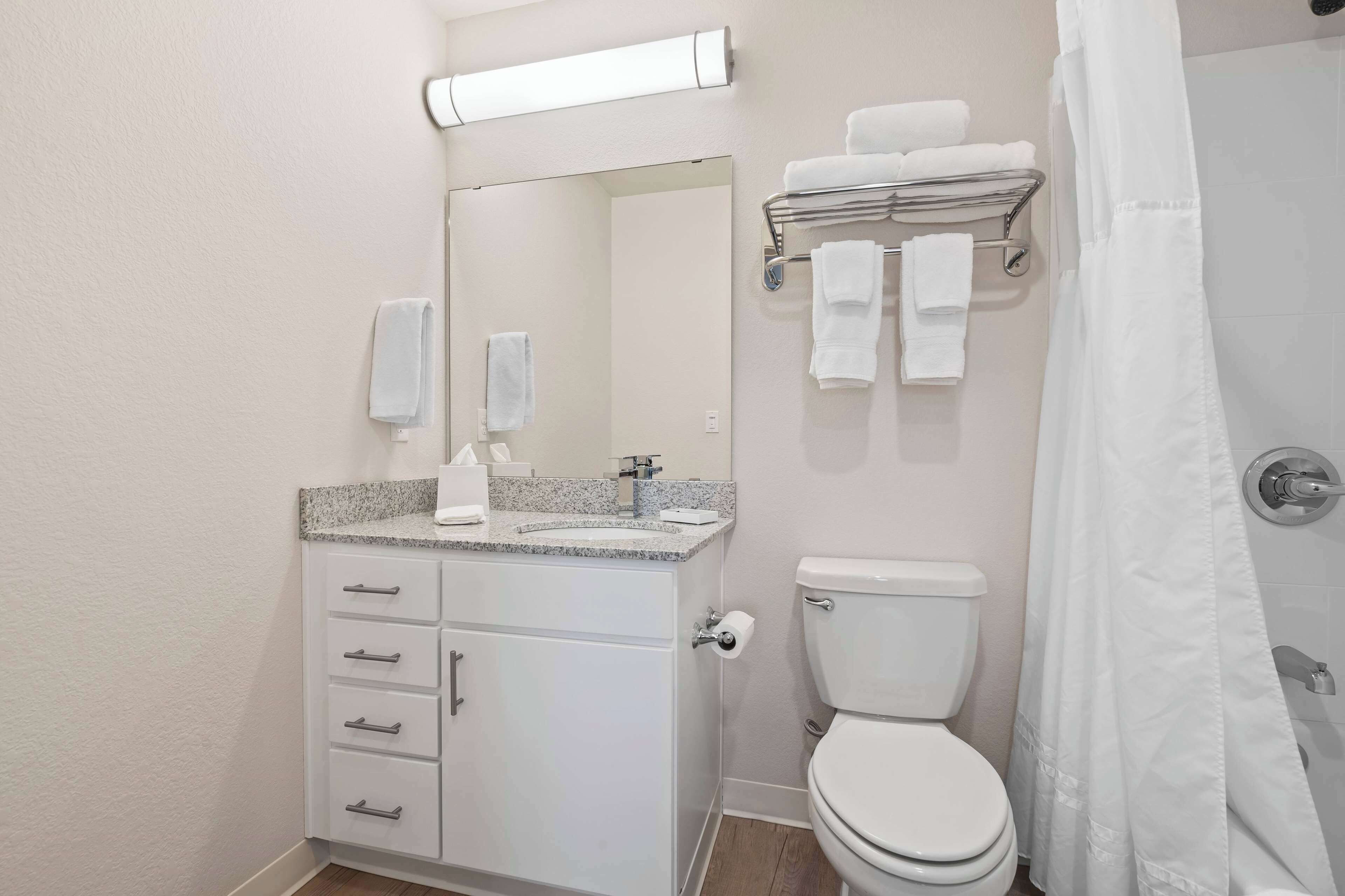 A bathroom with a white sink, mirror, and toilet. There are towels on a rack and a shower curtain.