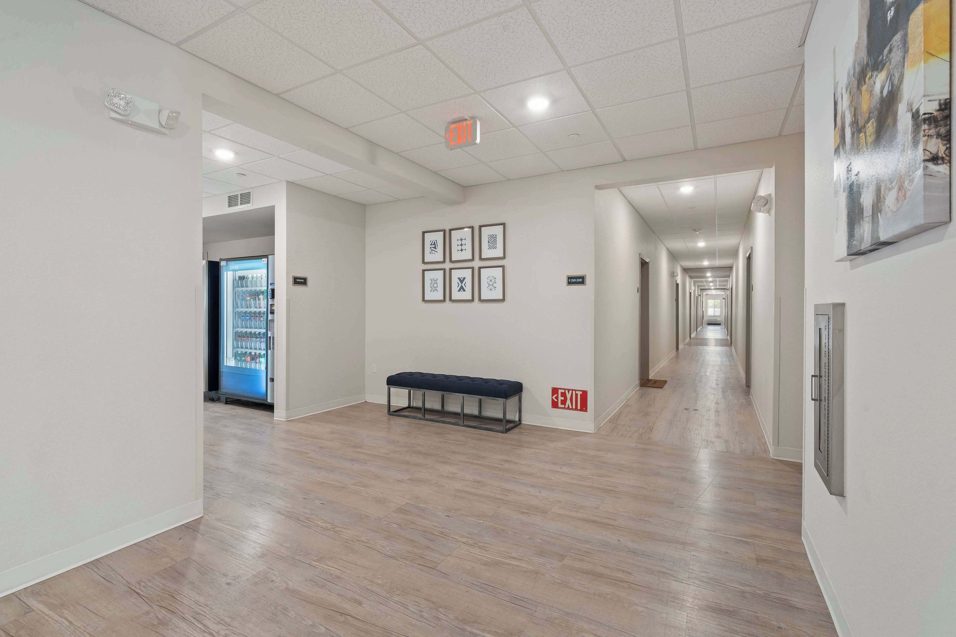 A modern hallway with a bench, framed artwork on the walls, and an exit sign.