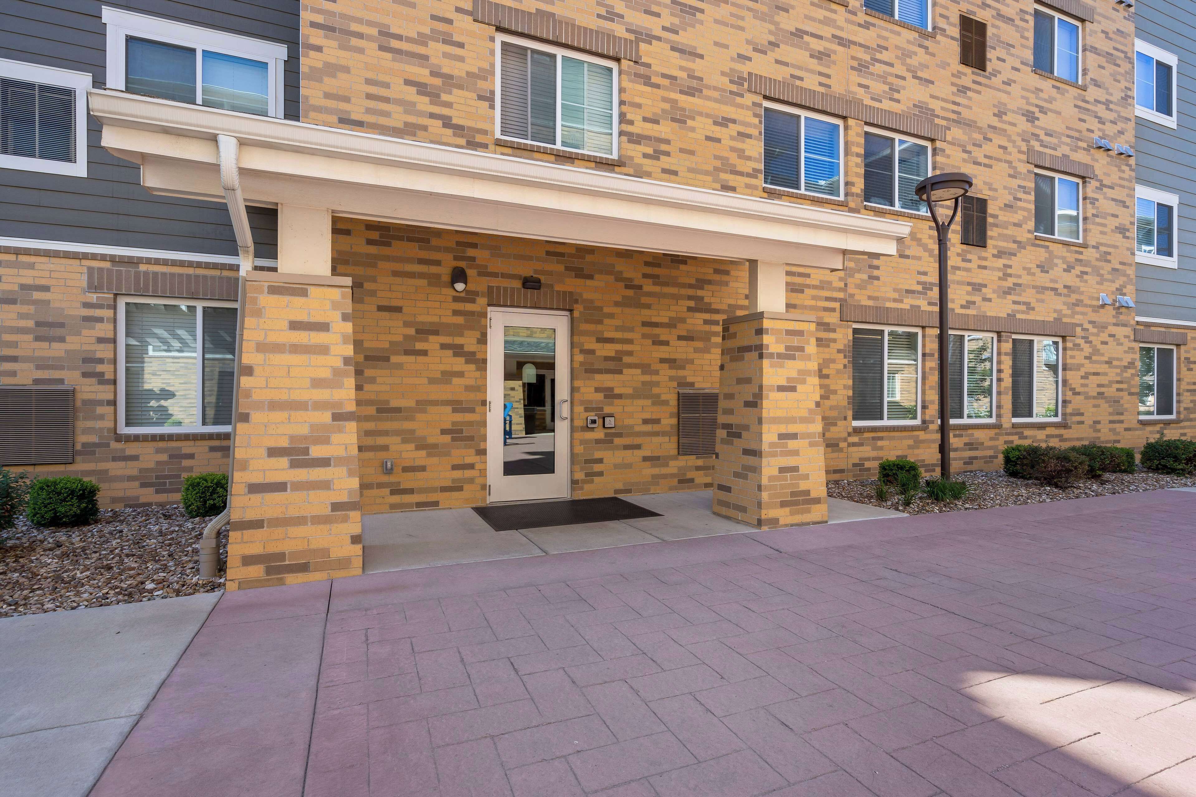 A multi-story residential building with a brick facade, a covered entrance, and a paved driveway.