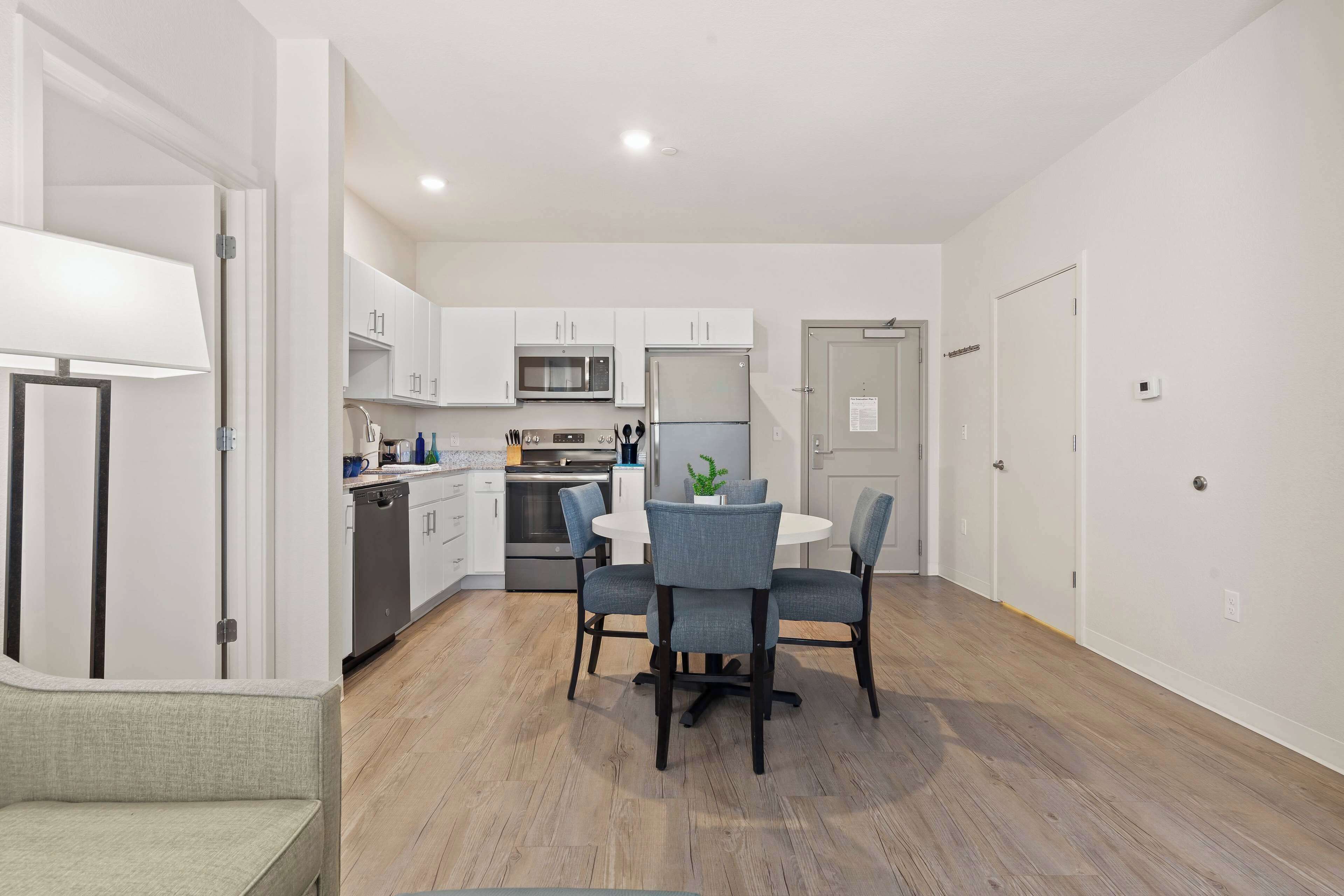 A modern kitchen with white cabinets, a microwave, a refrigerator, and a dining table with chairs.