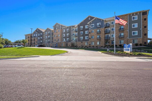 A multi-story hotel with a brick facade, a flagpole with an American flag, and a parking lot.