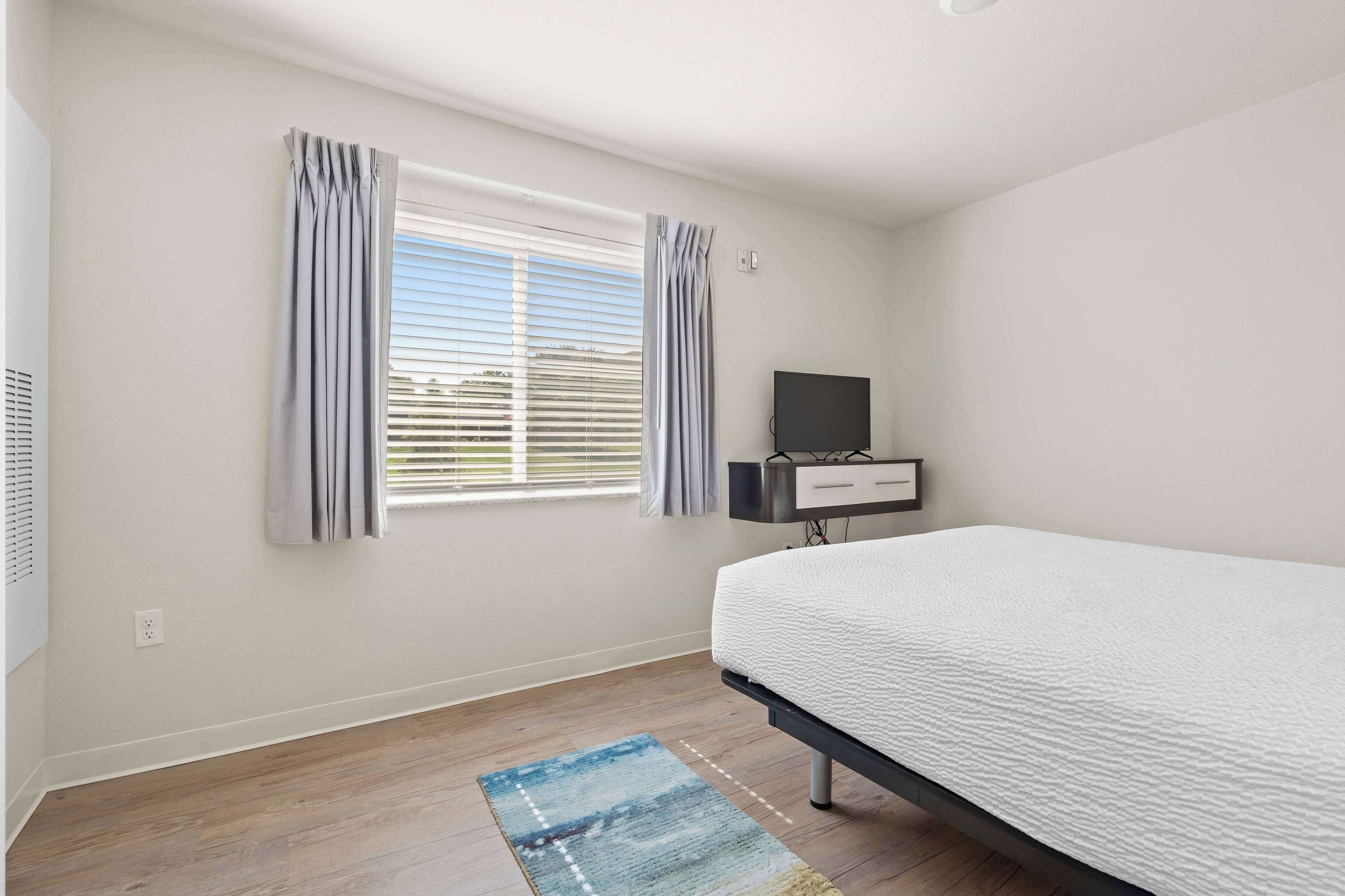 A bedroom with a bed, a TV, and a window with curtains.