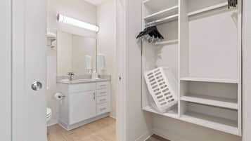 A modern bathroom with a toilet, sink, mirror, and storage shelves.