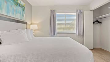 A hotel room with a large bed, a window with blinds, a lamp, and a wardrobe.