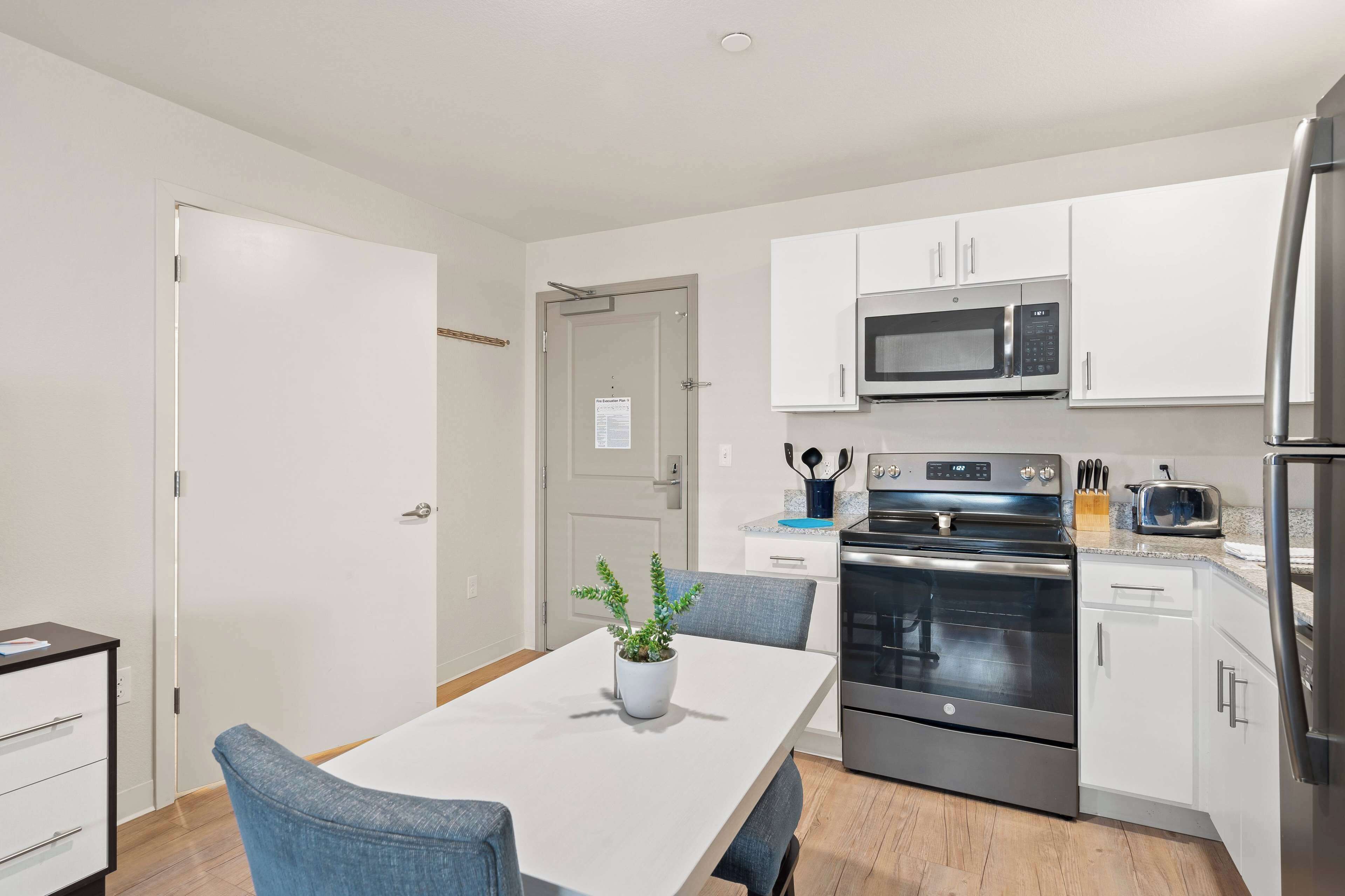 A modern kitchen with white cabinets, stainless steel appliances, and a dining area with a table and chairs.
