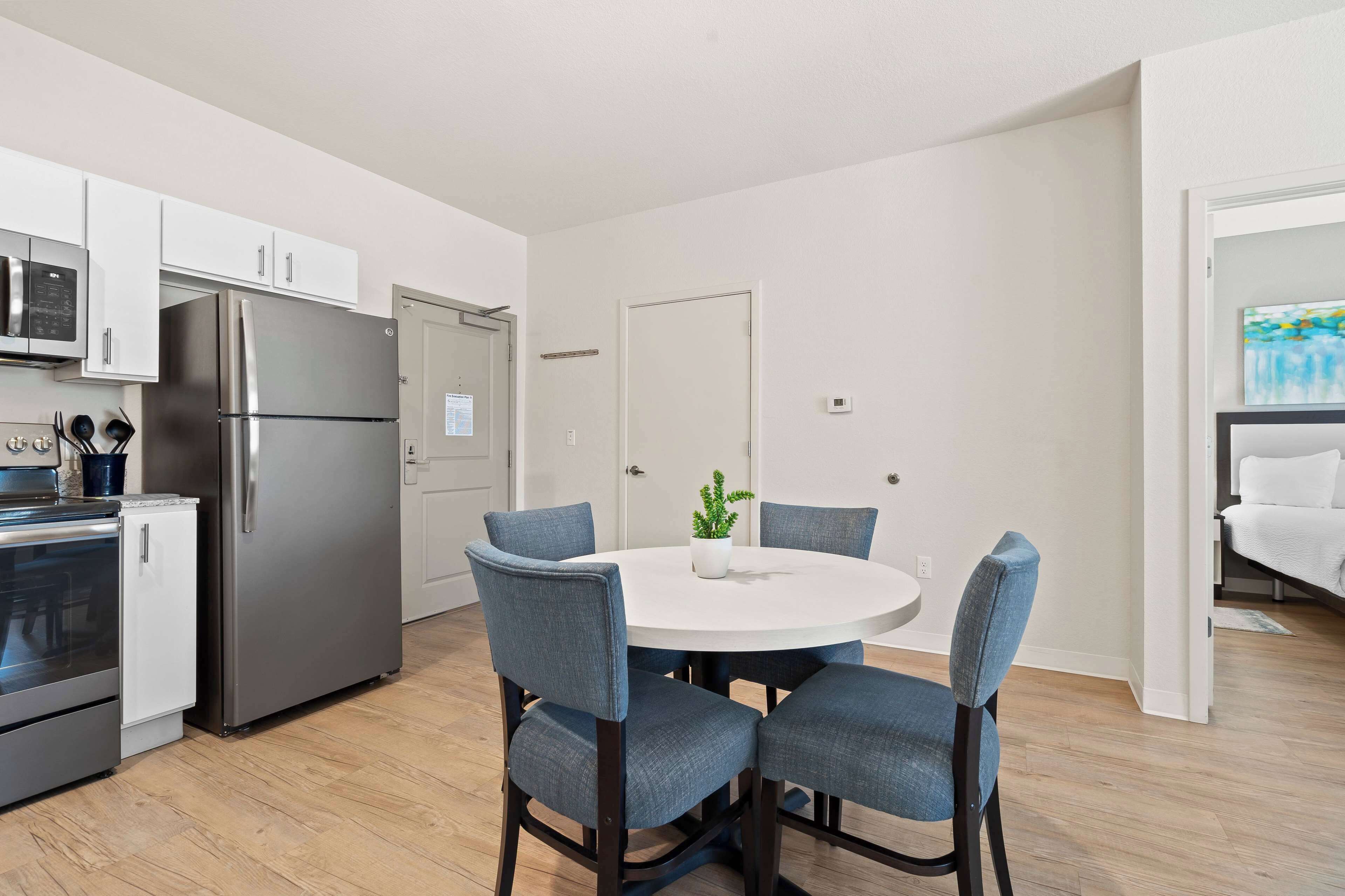 A modern kitchen with stainless steel appliances, a dining area with a round table and four chairs, and a small potted plant.