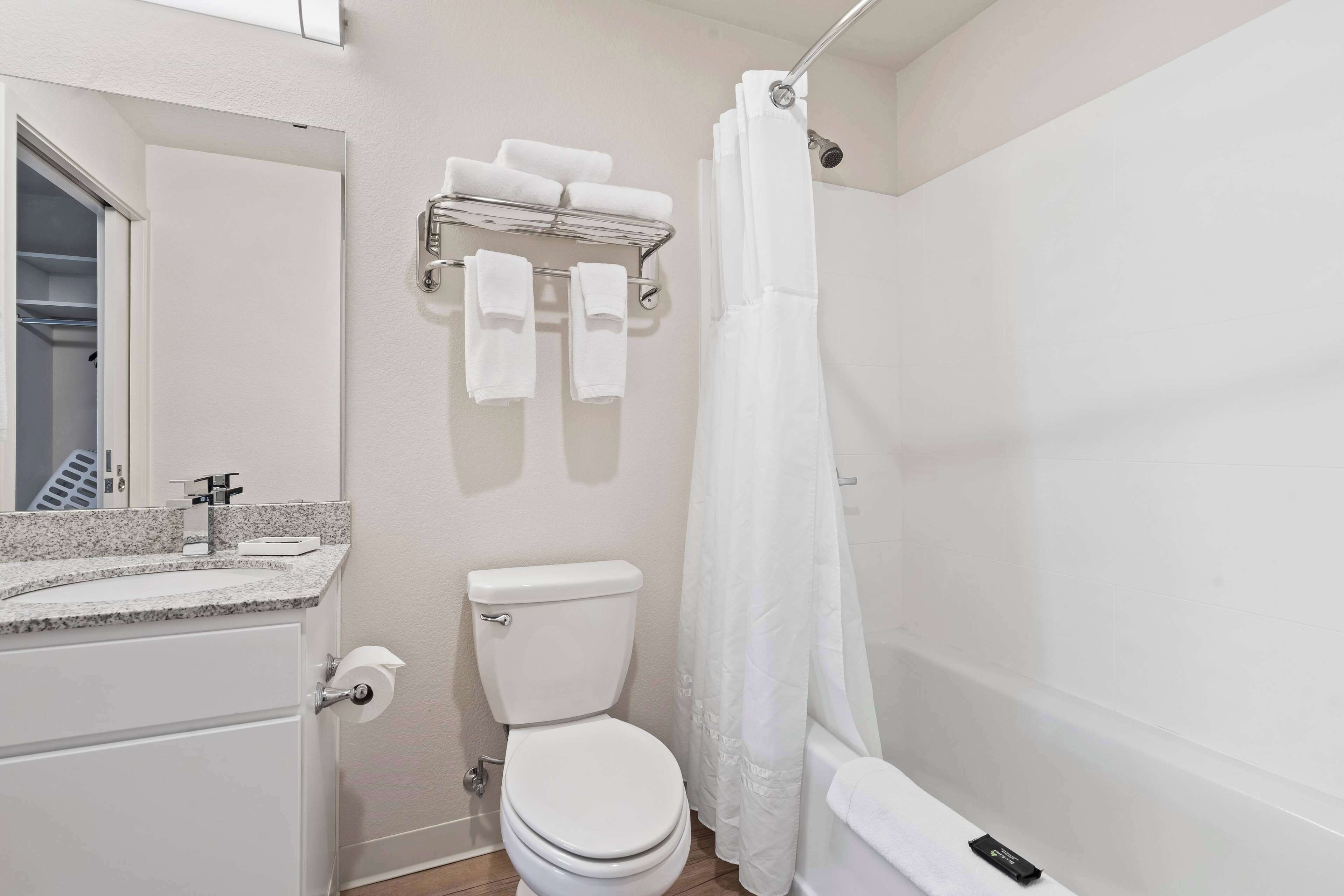 Un baño con inodoro, toallero con toallas, cortina de ducha y lavabo con grifo.