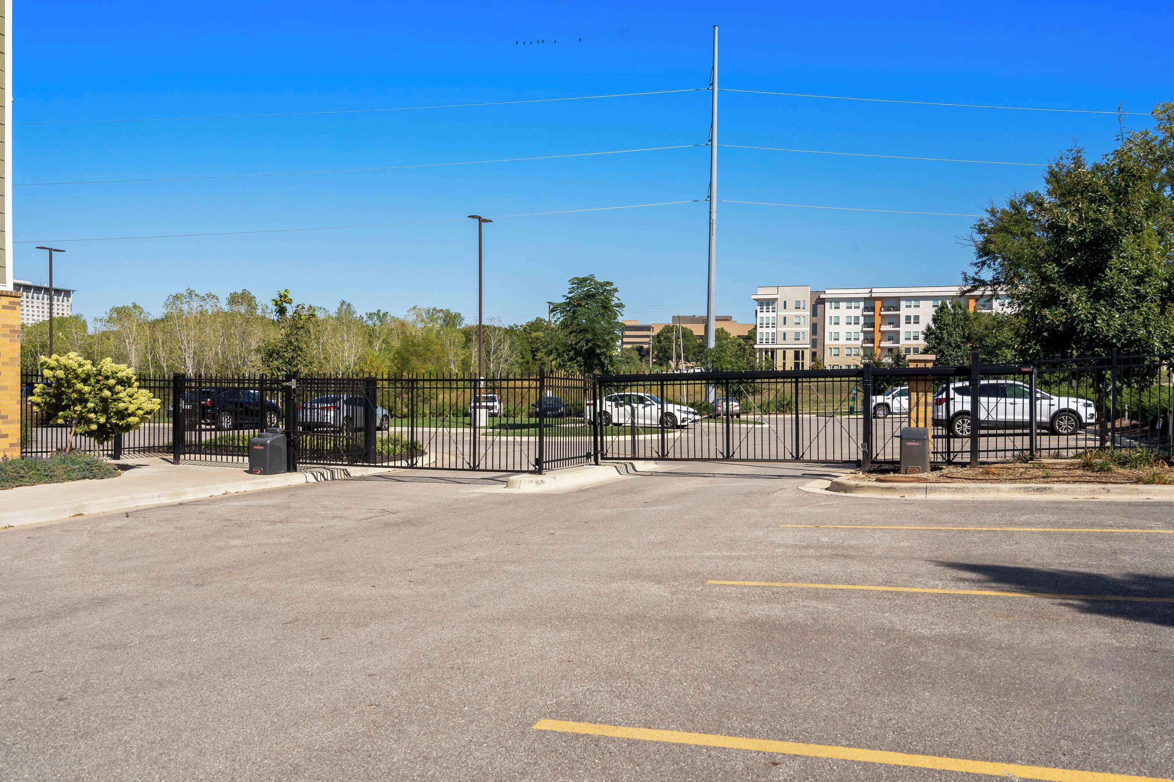 A parking lot with a black fence, a clear blue sky, and buildings in the background.