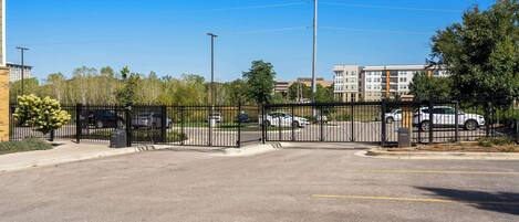 A parking lot with a black fence, a clear blue sky, and buildings in the background.
