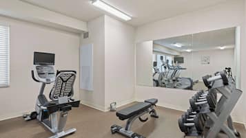 Un gimnasio con equipamiento de ejercicio, cinta de correr, pesas y un espejo.