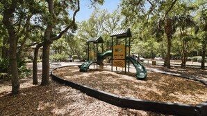A playground with a slide and climbing structure surrounded by trees. - Lyons 12 (Hilton Head Island)