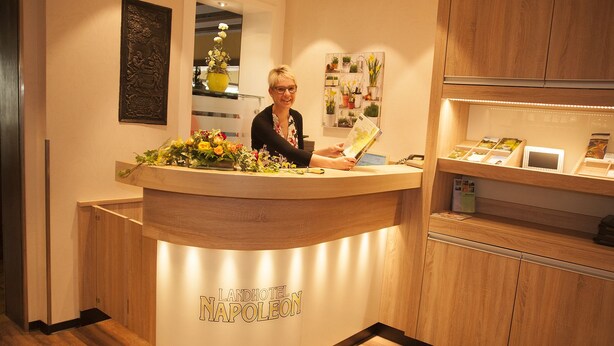 A reception desk with a sign reading "Landhotel Napoleon" and a woman behind it. - Landhotel Napoleon (Wipperfuerth)
