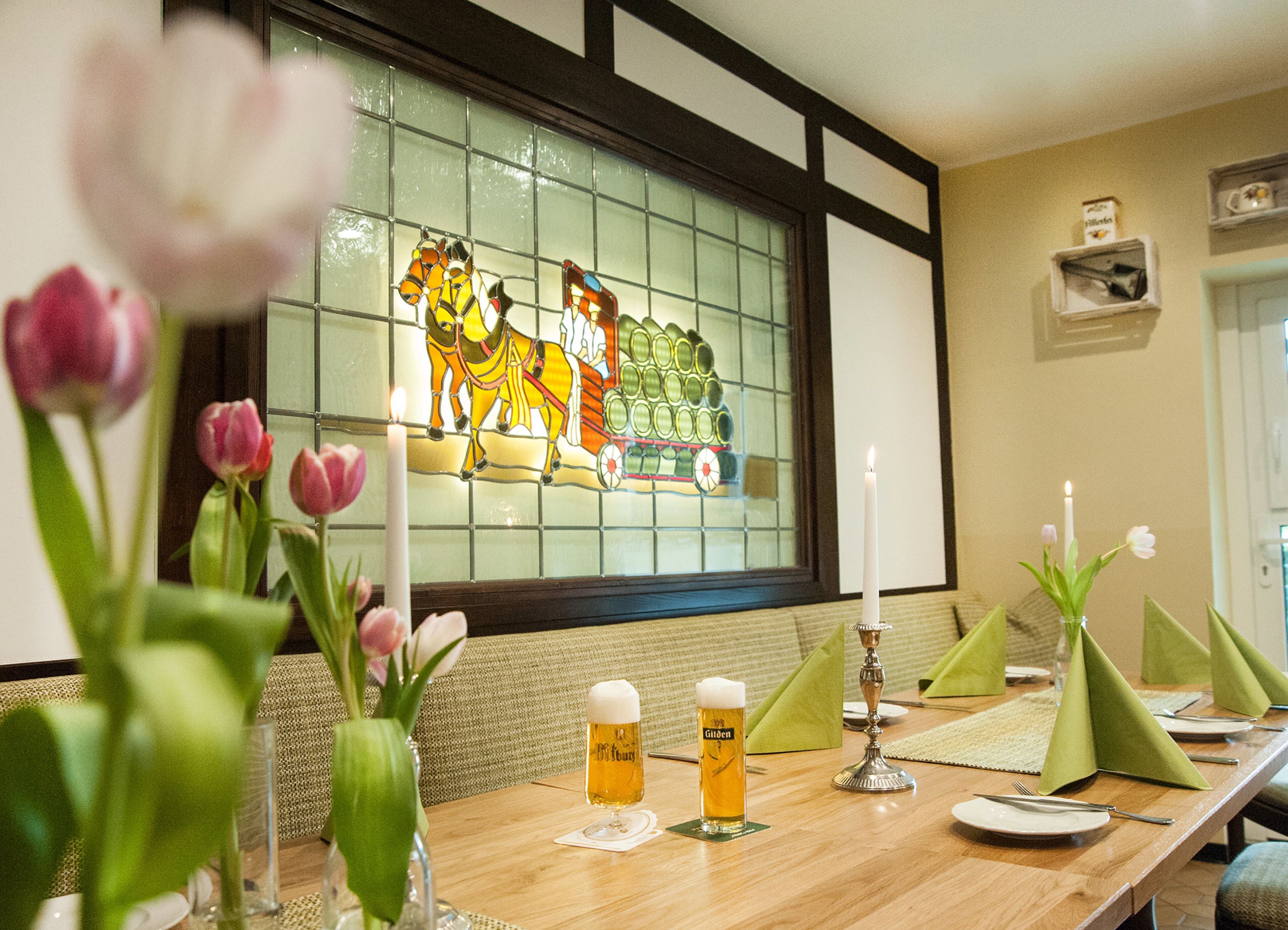 A dining table with a stained glass window, tulips, and a candle.