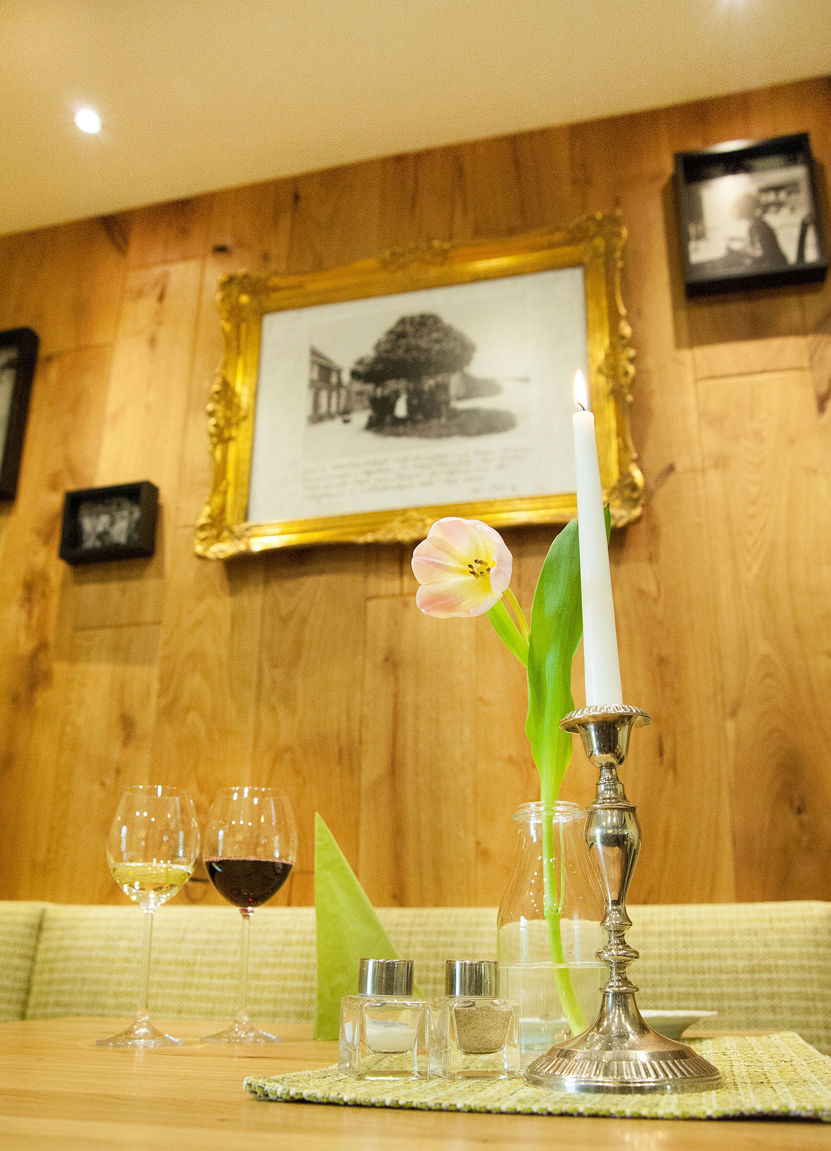 Une table à manger avec une bougie, une fleur, des salières et des poivrières, et des verres à vin.