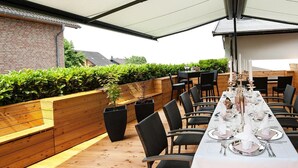 An outdoor dining area with a long table set for a meal, surrounded by chairs and a wooden deck. - Landhotel Napoleon (Wipperfuerth)