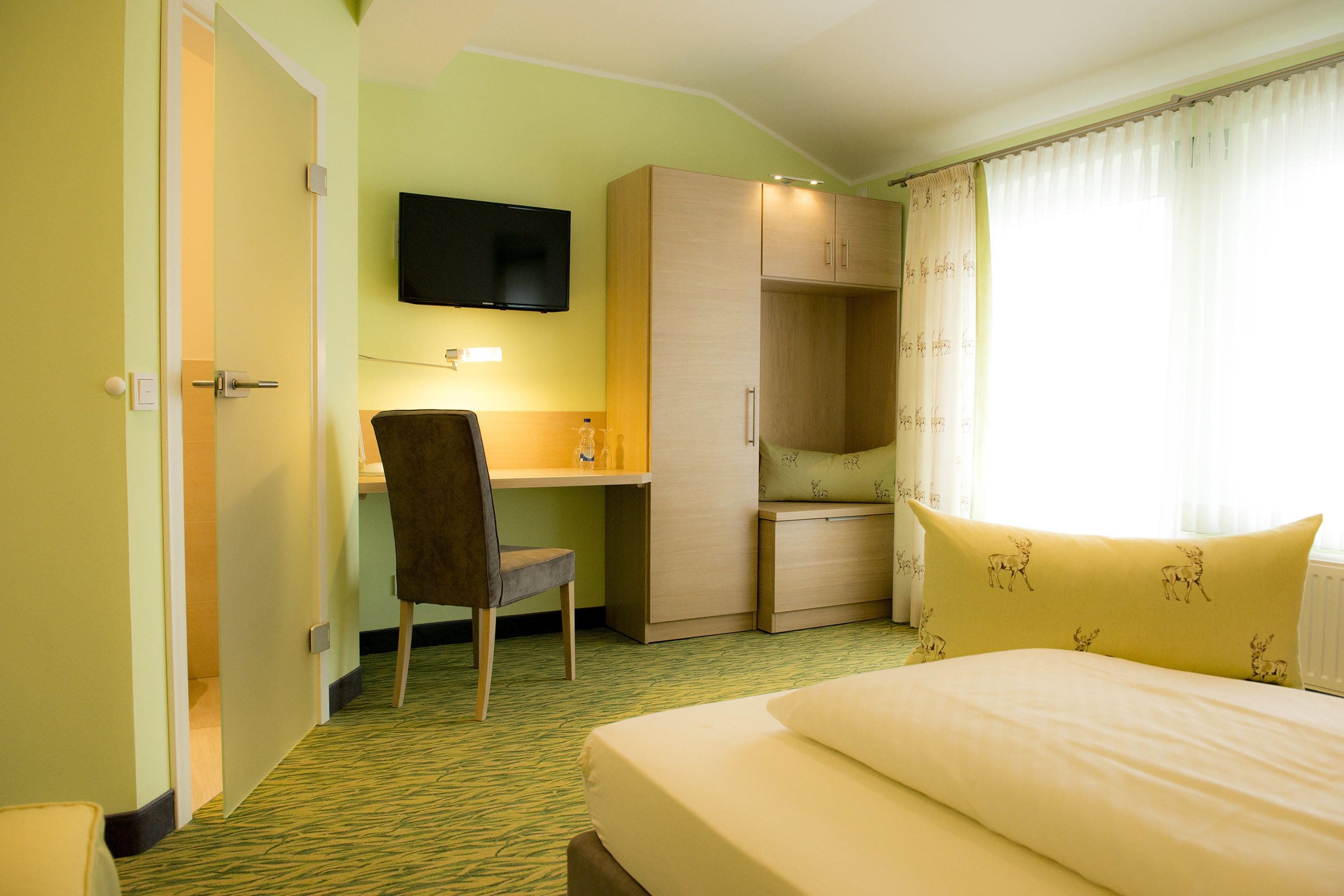 A hotel room with a bed, a desk, a chair, a television, and a wardrobe.