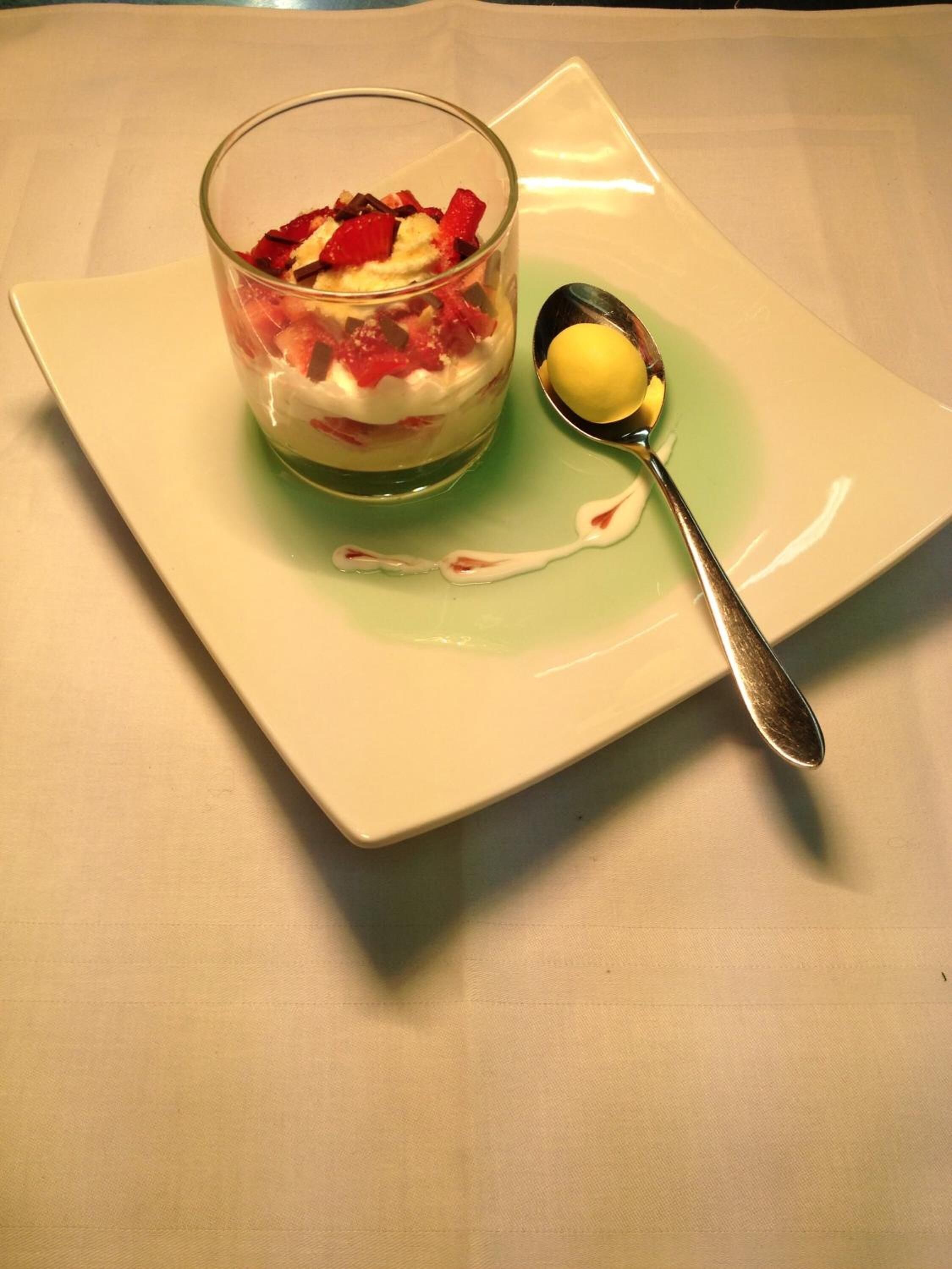 Un postre en un bol de vidrio sobre un plato cuadrado, con una cuchara a un lado.