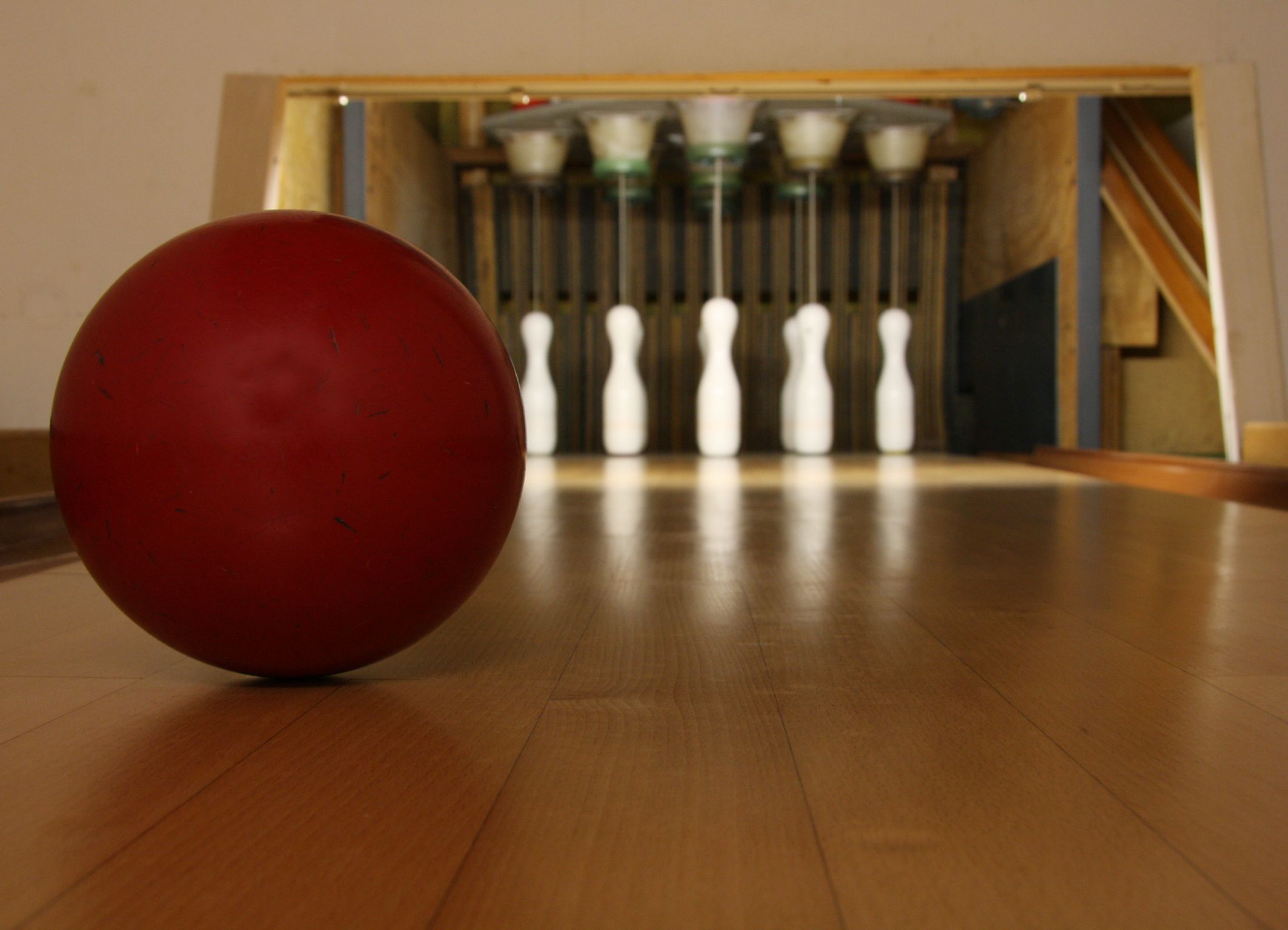 A bowling ball on a wooden floor with a bowling alley in the background.