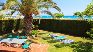 A patio with a table and chairs, a palm tree, and a view of the beach.