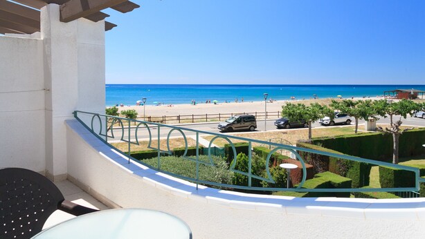 A balcony with a view of a beach, a street with parked cars, and a clear blue sky.