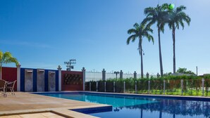 A swimming pool with a tiled deck, a red wall, and palm trees in the background.