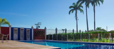 A swimming pool with a tiled deck, a red wall, and palm trees in the background.