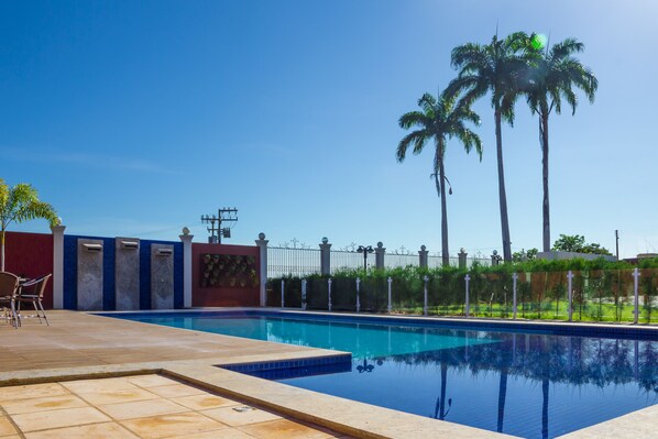 Una piscina con borde de baldosas, una pared roja y palmeras al fondo.