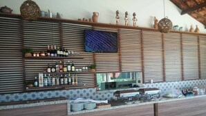 A bar area with a wooden counter, shelves with bottles, and a television mounted on the wall.