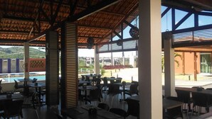 An outdoor dining area with tables and chairs, a pool in the background, and a view of the surrounding landscape.