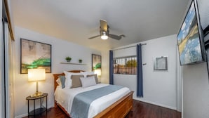 Un dormitorio con una cama de madera, un ventilador de techo, una mesita de noche con lámpara y obras de arte en las paredes.