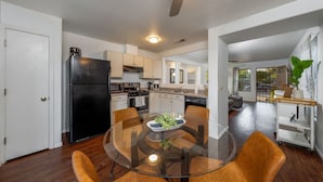 Una cocina moderna con un refrigerador negro, gabinetes blancos y una mesa de comedor de vidrio con sillas.