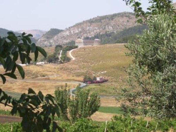 A view of a building with columns, surrounded by a hilly landscape and greenery. - Sun House (Calatafimi Segesta)